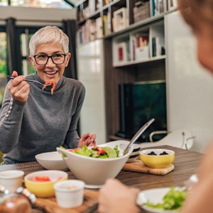 Woman with black glasses smiling while eating with friend