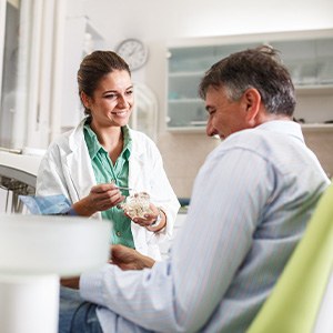 Smiling dentist showing patient model of teeth
