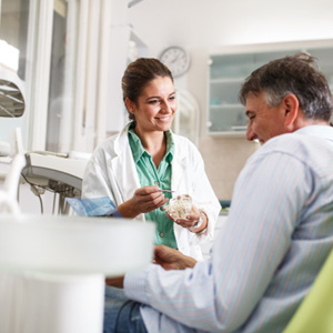 Smiling dentist showing patient model of teeth