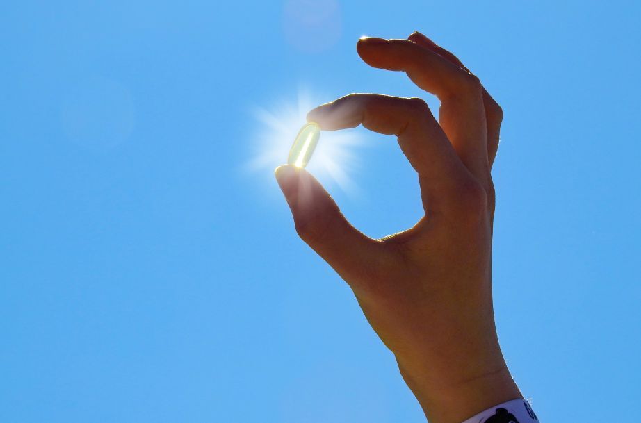 A hand holding a vitamin D capsule in the sun